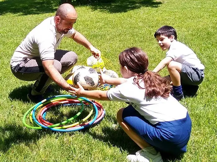 Profesor de educación física preparando material deportivo con alumnos en el parque