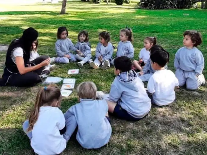 Niños de nivel inicial sentados en ronda sobre el pasto durante una clase al aire libre