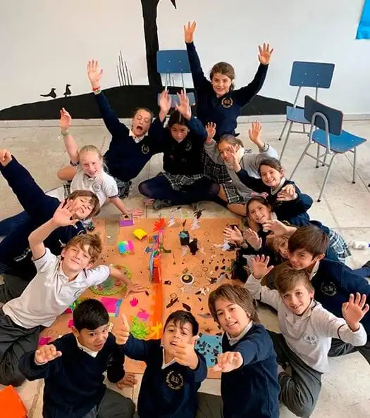 Alumnos de primaria celebrando con los brazos en alto alrededor de un proyecto grupal
